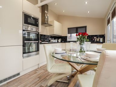 A kitchen with a glass dining table set with white dishes and red flowers at Sparrows Den Lodge in Winchelsea Beach