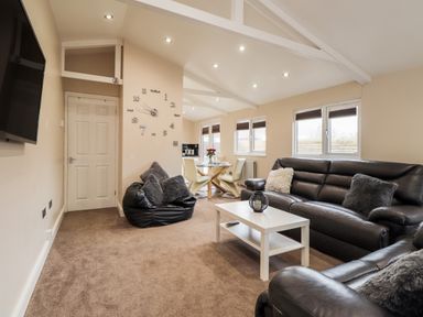 A living room with black leather sofas a white coffee table a bean bag a dining table and wall clock at Sparrows Den Lodge in Winchelsea Beach