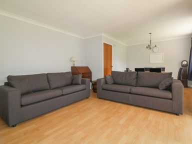 A living room with two gray sofas a wooden floor a wooden door a small wooden desk with a lamp and a dining area at Three Jays in Lanreath