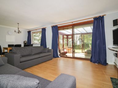 A living room with dark sofas wooden dining table and blue curtains at Three Jays in Lanreath