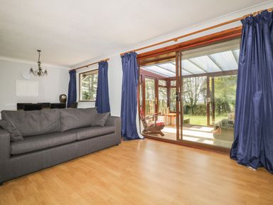 A living room with a gray couch wooden floor and dark blue curtains beside large sliding glass doors at Three Jays in Lanreath