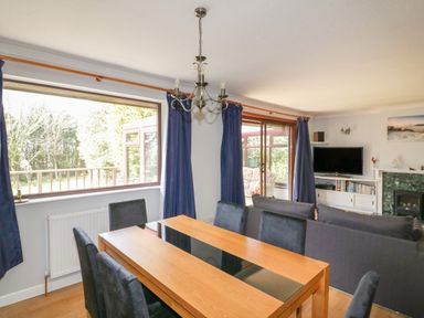 A dining area with a wooden table and six chairs next to a living room with a sofa television and fireplace at Three Jays in Lanreath