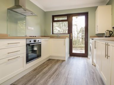 A kitchen with white cabinets a wooden countertop oven washing machine and glass door at Three Jays in Lanreath