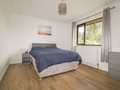 A bedroom with a bed a bedside table a chest of drawers and a window with curtains at Three Jays in Lanreath