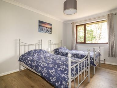 A bedroom with two single metal frame beds with blue floral bedding and a window with curtains at Three Jays in Lanreath