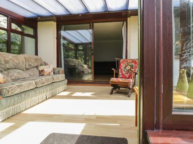 A conservatory with a floral sofa and a rocking chair at Three Jays in Lanreath
