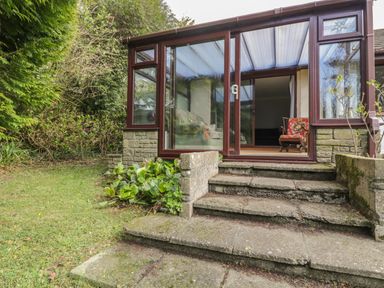 An outdoor stone staircase leading to a glass-enclosed porch with chairs inside at Three Jays in Lanreath