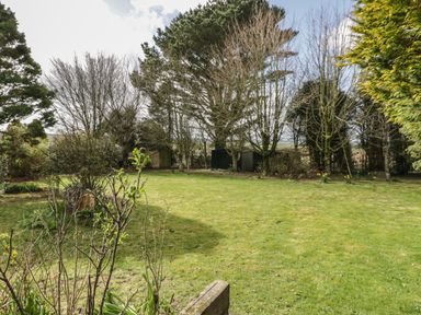 A garden with a lawn surrounded by trees and shrubs at Three Jays in Lanreath