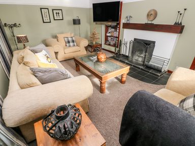 A living room with beige sofas a wooden coffee table a fireplace and a wall mounted television at Mountain Farm in Broad Haven