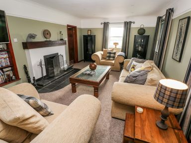 A living room with beige sofas a wooden coffee table a fireplace and a lamp on a wooden side table at Mountain Farm in Broad Haven