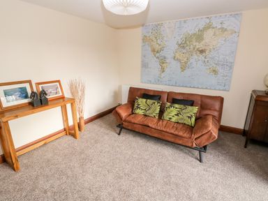 A room with a brown sofa with cushions a wooden table with framed pictures and decorative items and a world map on the wall at Mountain Farm in Broad Haven