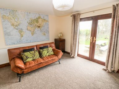 A room with a brown leather sofa with pillows a world map on the wall a small cabinet with a globe and glass doors with curtains at Mountain Farm in Broad Haven