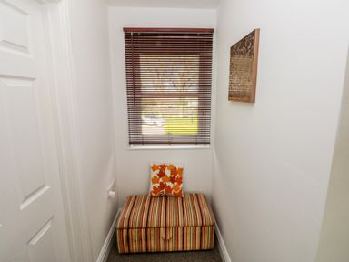 A small room with a striped ottoman and a cushion in front of a window with wooden blinds at Mountain Farm in Broad Haven