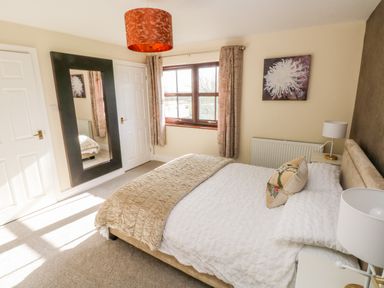 A bedroom with a bed a large mirror a window with curtains and bedside tables at Mountain Farm in Broad Haven