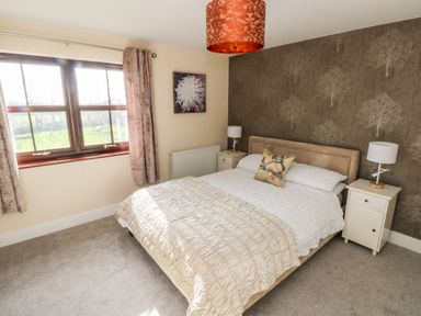 A bedroom with a bed between two bedside tables and a window with curtains at Mountain Farm in Broad Haven