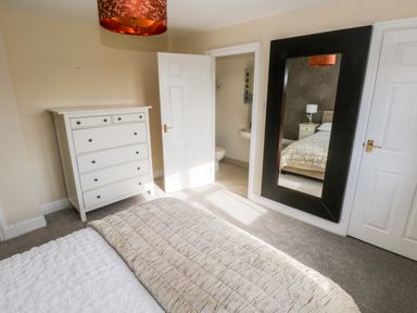 A bedroom with a bed and dresser and open door showing bathroom and a large wall mirror at Mountain Farm in Broad Haven