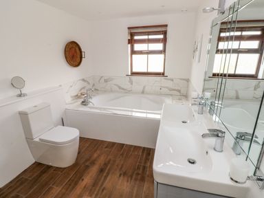 A bathroom with a toilet a bathtub a double sink and wooden floor at Mountain Farm in Broad Haven