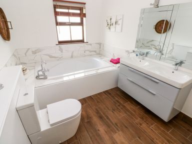 A bathroom with a bathtub a toilet and a double sink vanity with mirror at Mountain Farm in Broad Haven