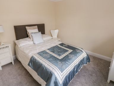 A bedroom with a double bed covered with white and blue bedding a white nightstand with a lamp and a white chair at Mountain Farm in Broad Haven