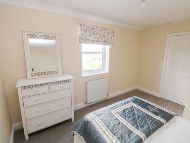 A bedroom with a bed a white dresser with mirror a window and a closed door at Mountain Farm in Broad Haven