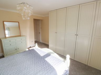 A bedroom with a bed a chest of drawers with a mirror and built in wardrobes at Mountain Farm in Broad Haven