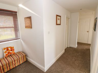 A hallway with a window and wooden blinds a striped bench with a leaf patterned pillow and three doors at Mountain Farm in Broad Haven