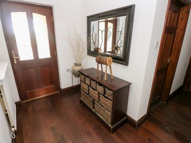 A hallway with a wooden door a wicker basket cabinet a decorative wooden reindeer a large mirror and a vase with dried plants at Mountain Farm in Broad Haven