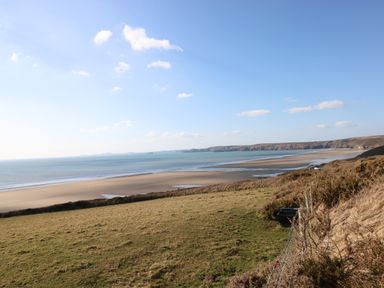 A coastal landscape with a sandy beach and grassy fields under a blue sky at Mountain Farm in Broad Haven