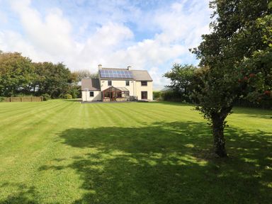 A large house with solar panels on the roof and a conservatory surrounded by a mowed lawn and trees at Mountain Farm in Broad Haven