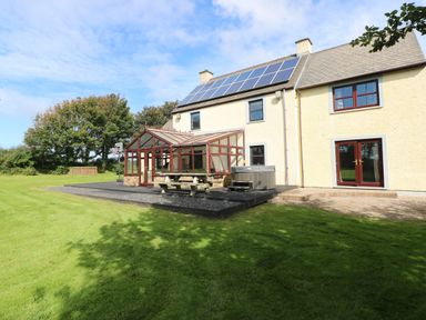 A house with solar panels on the roof a glass conservatory a picnic table a hot tub and a basketball hoop on a lawn at Mountain Farm in Broad Haven