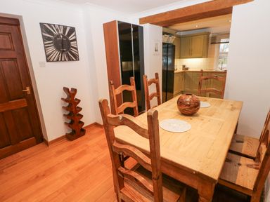 A dining area with wooden table and chairs and a kitchen in the background at Mountain Farm in Broad Haven