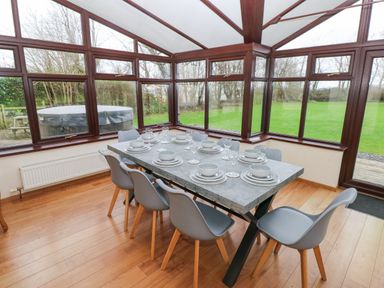 A dining area with a table set for eight and large windows showing a green lawn at Mountain Farm in Broad Haven
