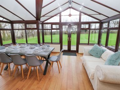 A conservatory dining area with a table set for eight and a sofa with cushions at Mountain Farm in Broad Haven