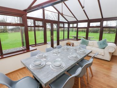 A dining area with a table set for eight and a sofa with cushions in a glass conservatory at Mountain Farm in Broad Haven