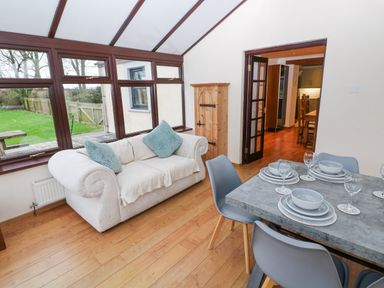 A sitting area with a white sofa next to large windows and a dining table set with plates and glasses at Mountain Farm in Broad Haven