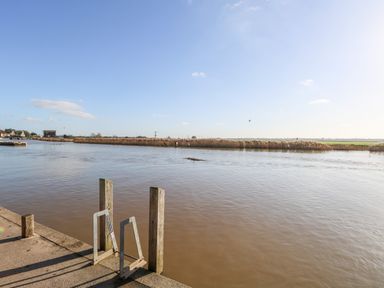 A river with wooden posts and metal railings and reed plants along the opposite bank at Foundry Cottage in Reedham