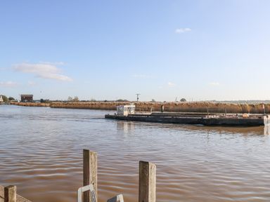 A river with a flat barge in the water and reeds along the riverbank at Foundry Cottage in Reedham