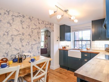 A kitchen with a wooden dining table and chairs next to blue cabinets and a window at Foundry Cottage in Reedham