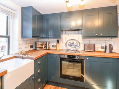 A kitchen with blue cabinets wooden countertops a white farmhouse sink oven microwave toaster and kettle at Foundry Cottage in Reedham