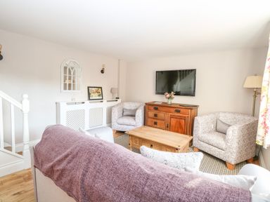A living room with armchairs a wooden coffee table a television on a wooden cabinet and a staircase at Foundry Cottage in Reedham