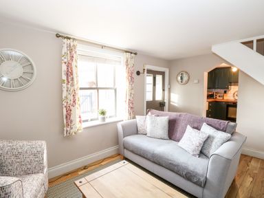A living room with a grey sofa and patterned armchair near a window and door at Foundry Cottage in Reedham