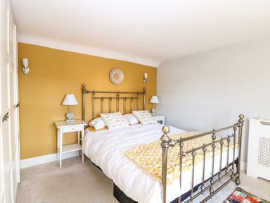 A bedroom with a metal bed frame bedside tables lamps and a yellow accent wall at Foundry Cottage in Reedham