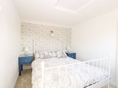 A bedroom with a white metal bed frame blue nightstands and patterned wallpaper at Foundry Cottage in Reedham