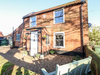 Exterior view of a brick cottage with white door and windows a gravel yard and a bench at Foundry Cottage in Reedham