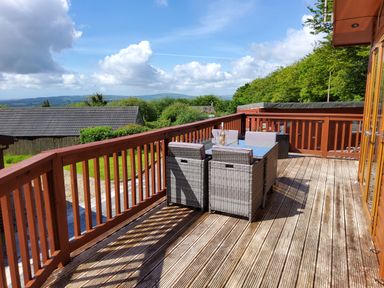 An outdoor wooden deck with a dining table and chairs overlooking greenery and hills at Lodge 11 in Tavistock