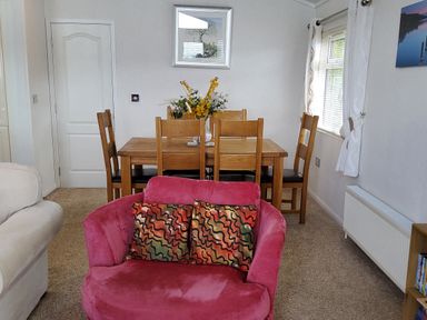 A dining area with wooden table and chairs and a pink armchair with cushions at Lodge 11 in Tavistock