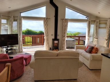 A living room with sofas a television and a stove with large windows overlooking a deck at Lodge 11 in Tavistock