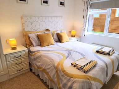 A bedroom with a double bed with pillows and folded towels on the bed between two bedside tables with lamps at Lodge 11 in Tavistock