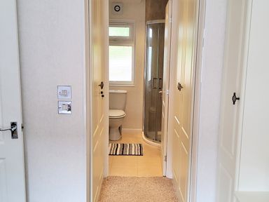 A narrow hallway leading to a bathroom with a toilet shower and window at Lodge 11 Tavistock