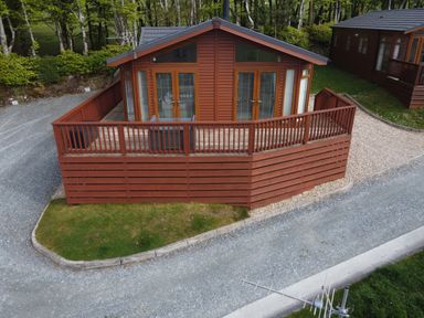 A wooden cabin with a fenced deck on a gravel and grass lot near trees at Lodge 11 in Tavistock